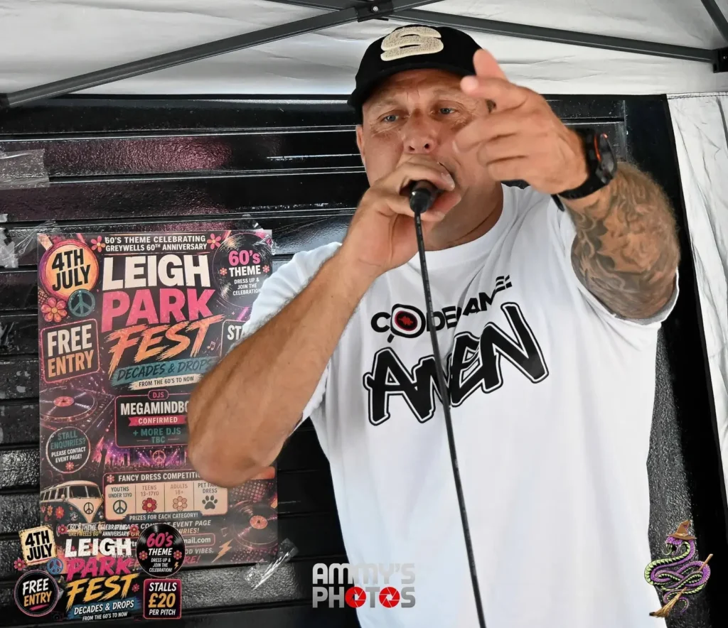 Performer holding a microphone and pointing towards the camera under a canopy.