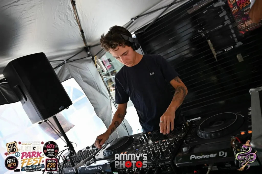 DJ in a dark T-shirt working at the mixing desk beside a speaker.