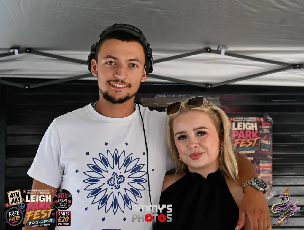 Two visitors posing together under a canopy, one wearing headphones.
