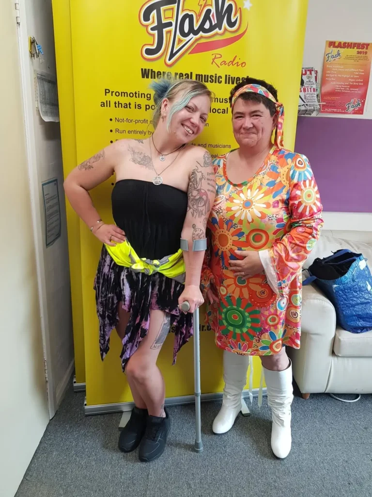 Two visitors posing in front of a yellow Flash Radio banner.
