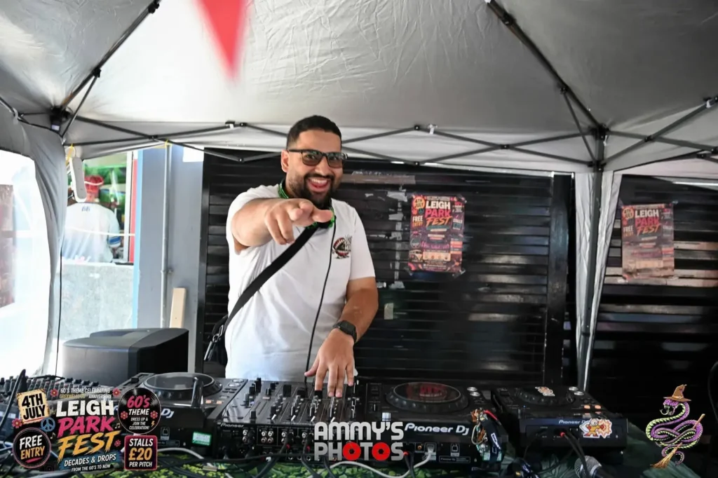 DJ smiling and pointing towards the camera from behind the mixing desk.